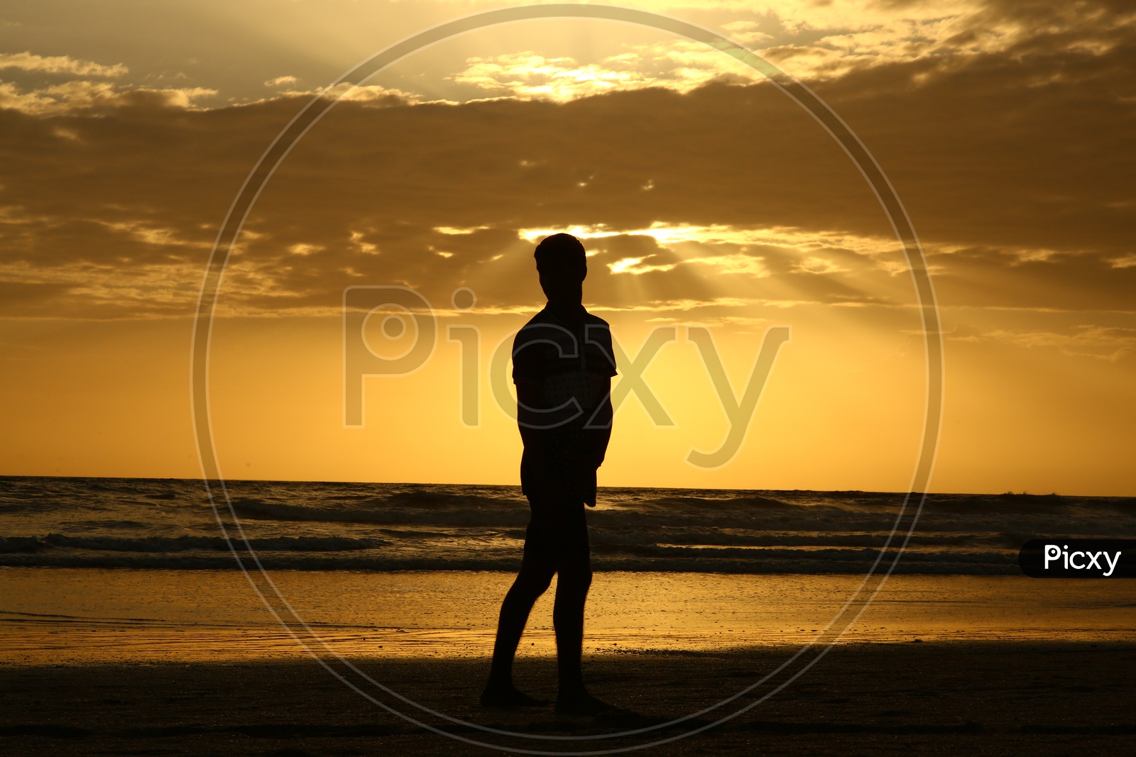 Silhouette of a Young Boy Standing At a Beach With Golden Sunset Sky In Background