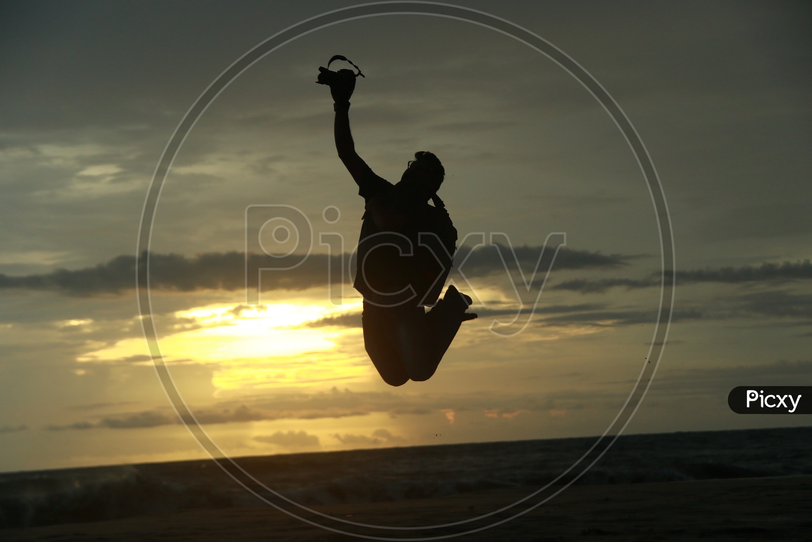 Silhouette Of a Photographer Jumping in Joy At a Beach Over Sunset Sky In Background