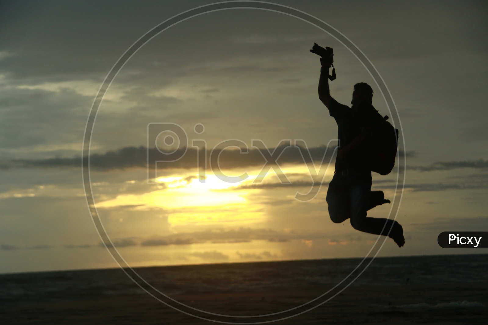 Silhouette Of a Photographer Jumping in Joy At a Beach Over Sunset Sky In Background