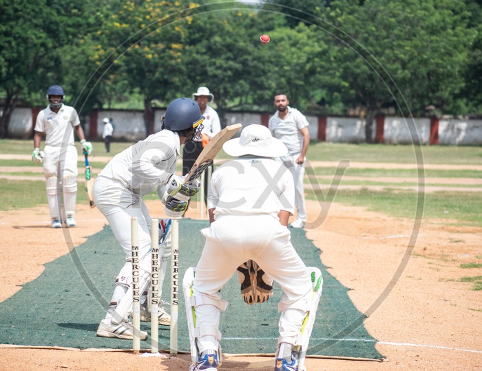 Cricket pitch with batsmem, bowler, empire and wicketkeeper in action