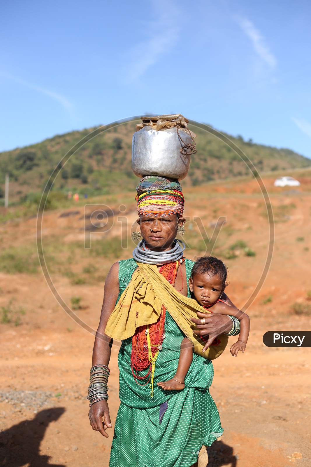 Bonda Tribal Woman Carrying Water Vessel And Her Child And Walking along Tribal Village Roads