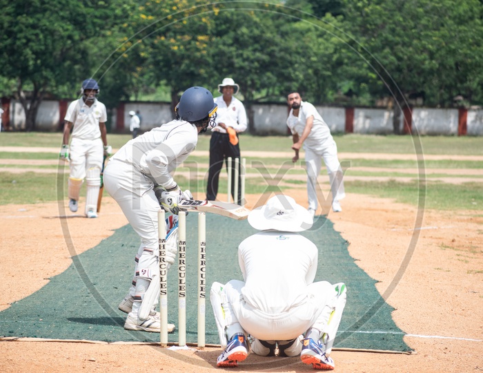 Cricket pitch with batsmem, bowler, empire and wicketkeeper in action