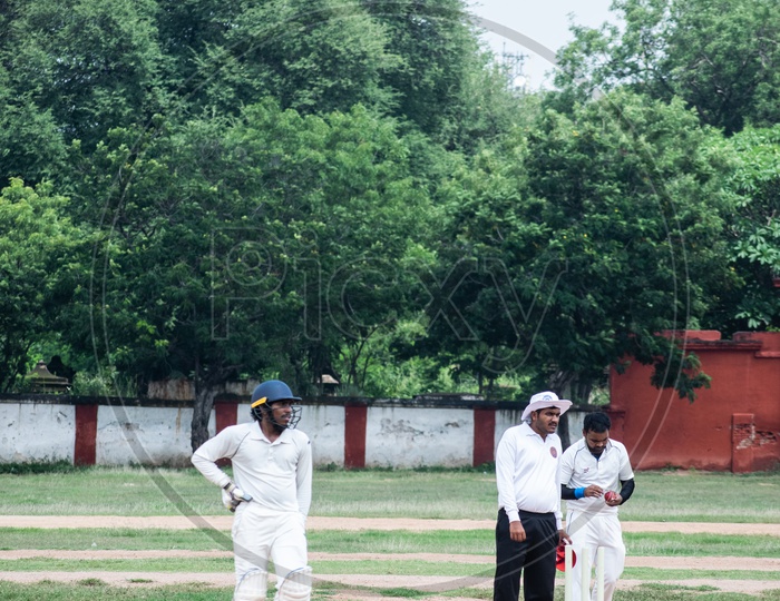 A bowler is bowling on the Cricket field while the empire watch and the batsman ready to take a run