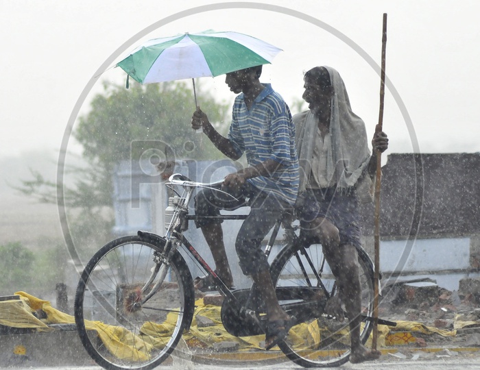 Indian boy riding bicycle holding umbrella during rain