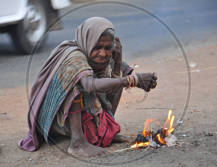 Indian Old homeless woman making a fireplace with trash