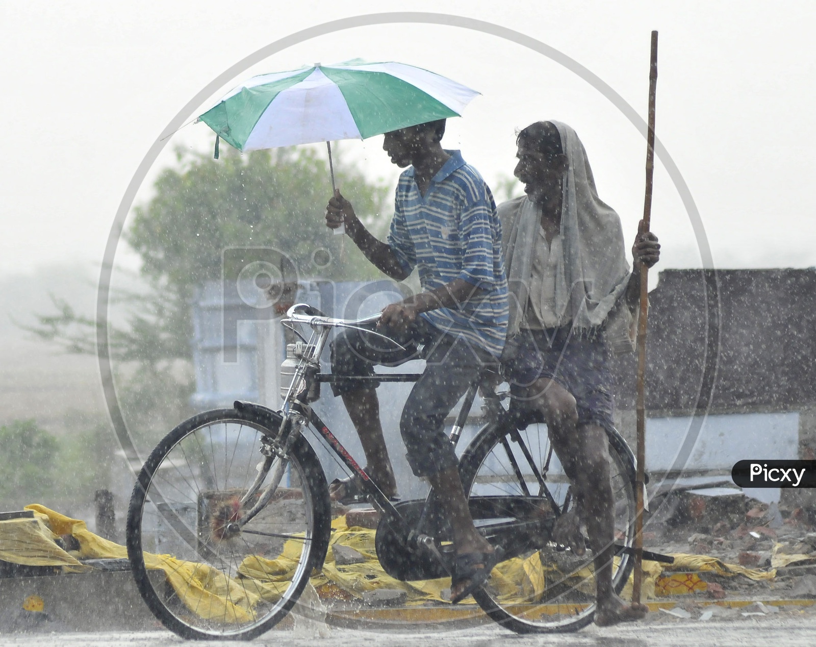 Indian boy riding bicycle holding umbrella during rain