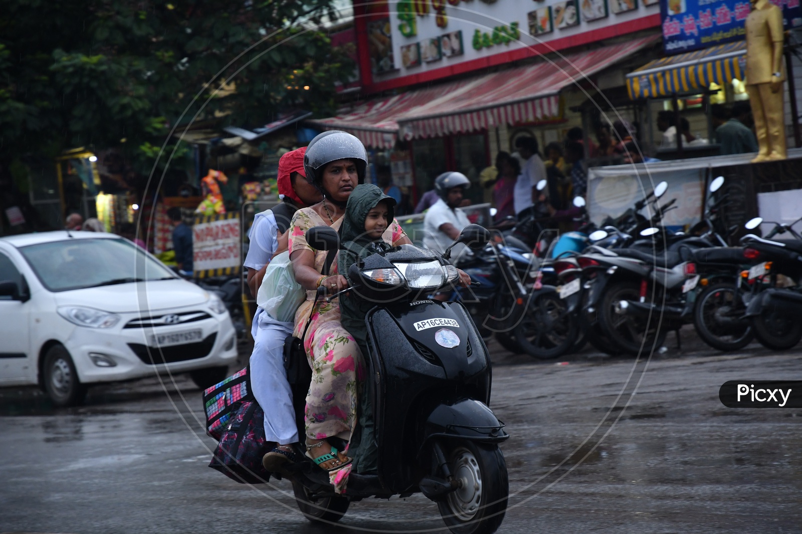 A Mother with her Children going on Scooty while raining