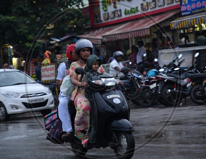 A Mother with her Children going on Scooty while raining