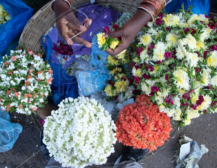 A Woman Flower Vendor Making Garlands With Flowers And Thread At a Flower Market