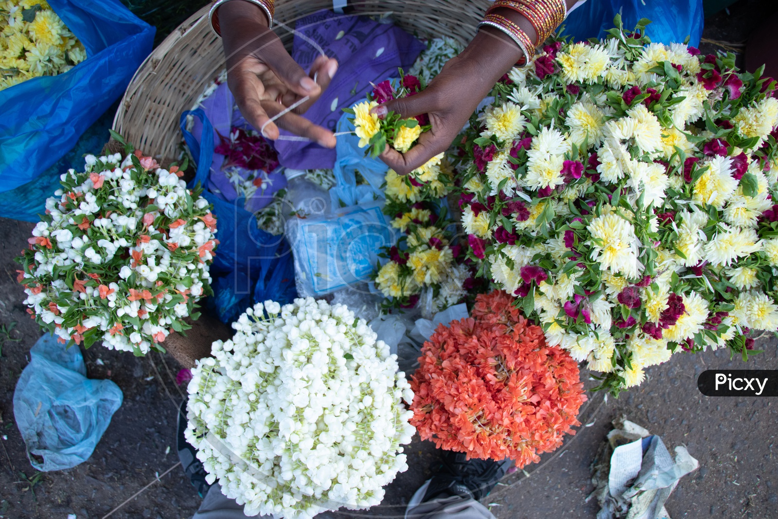 A Woman Flower Vendor Making Garlands With Flowers And Thread At a Flower Market