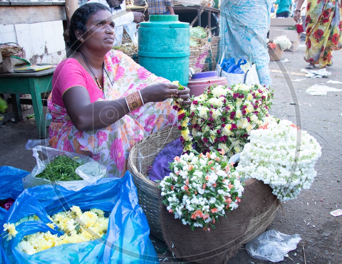 A Woman Flower Vendor With Flower Garland Piles At a Flower Market