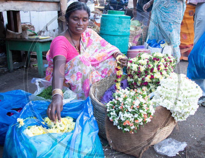 A Woman Flower Vendor With Flower Garland Piles At a Flower Market