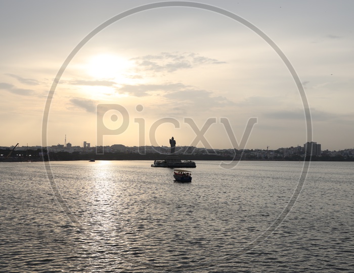 Silhouette Of  Buddha Statue In Hussain Sagar Lake With Telangana Tourism Boat  and Sunset Sky In Background