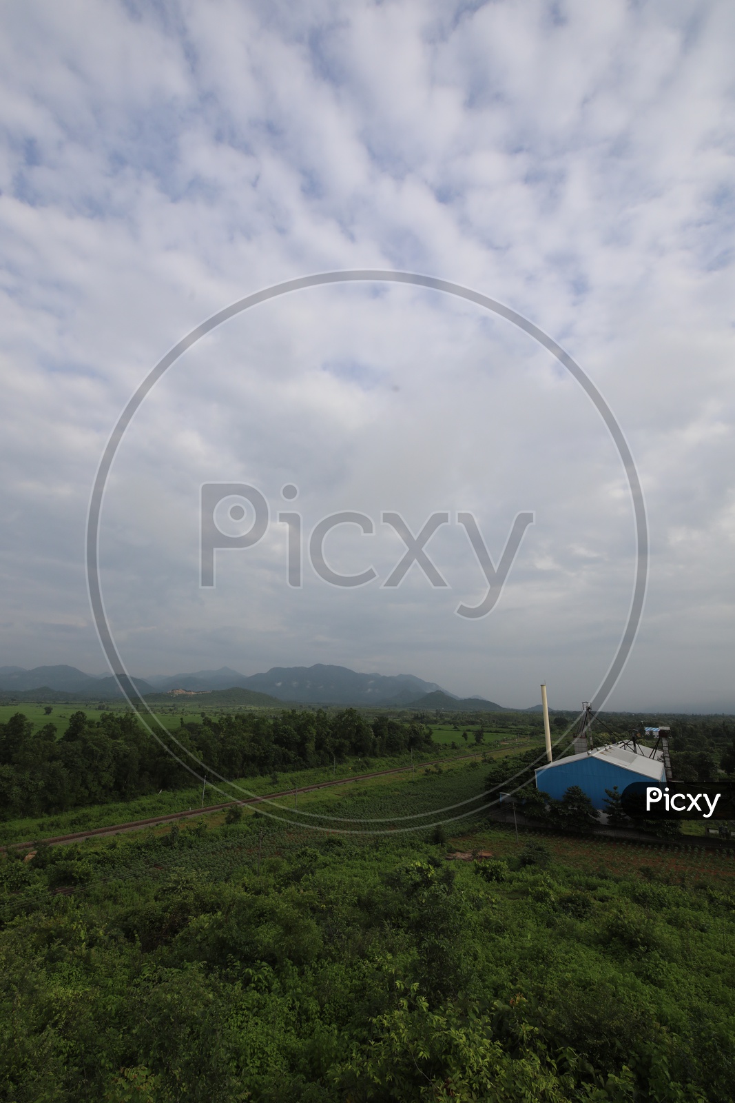 Railway Track Line Between Green Fields And Terrains With Blue Sky And Cotton Cloud Background