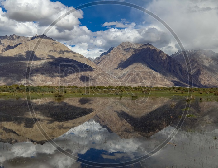 River Valley With Snow Mountains And Blue Sky With Cotton Clouds And Its reflection On Water Surface At Ladakh
