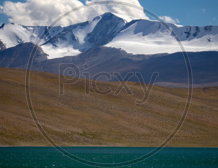 A View Of River Channel And Mountains With Blue Sky And Cotton Clouds In Background