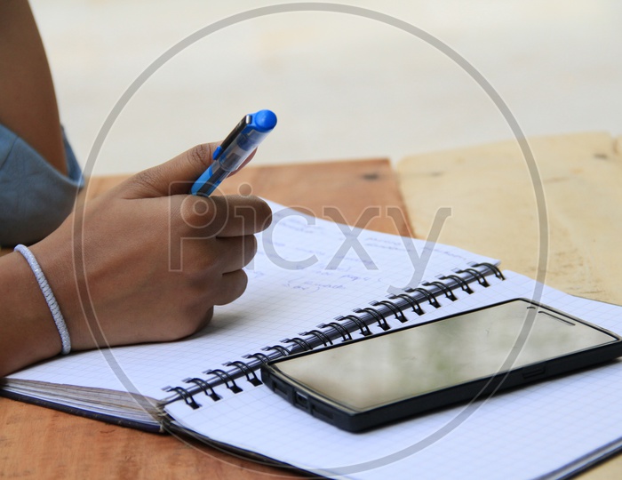 Image of Student Taking Notes In a Notebook And Smartphone on a Wooden ...