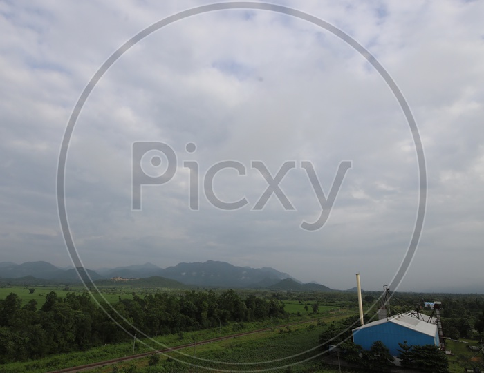 Railway Track Line Between Green Fields And Terrains With Blue Sky And Cotton Cloud Background