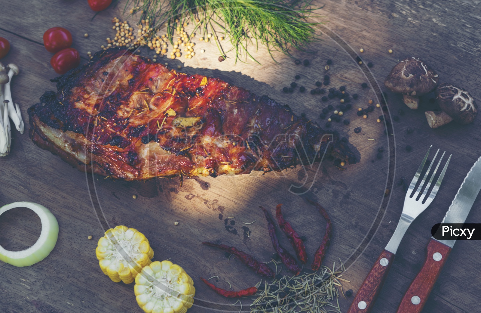 Top view of spicy hot grilled spare ribs from a summer BBQ served with a hot chili pepper and fresh tomatoes on an old vintage wooden cutting board