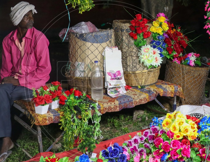 An old man selling artificial flowers on a roadside