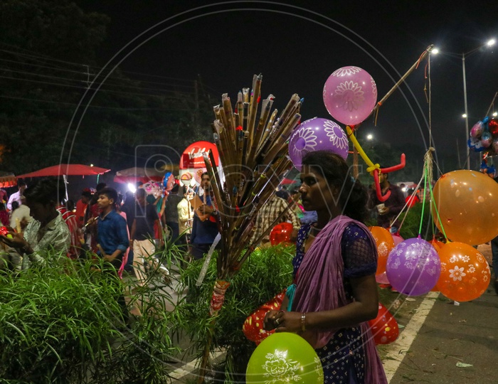 Women street vendor selling flutes and balloons in a busy night market