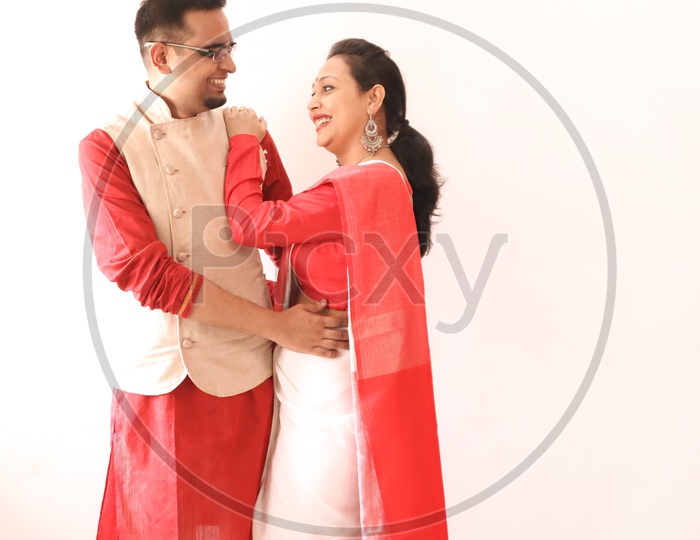 A Young Indian Bengali Assamese Married Romantic Couple Dressed In Red And White Ethnic Indian Dress, Looking At Each Other And Smiling