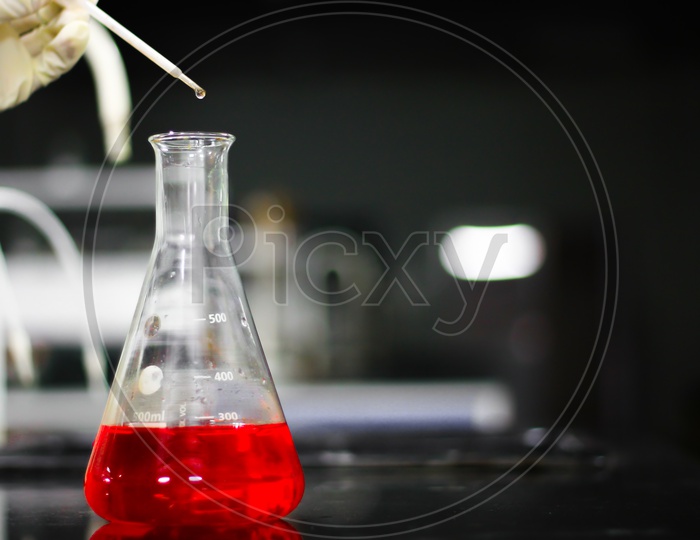 Pouring A Red Chemical On A Glass Conical Flask With A Dropper In A Chemistry Lab