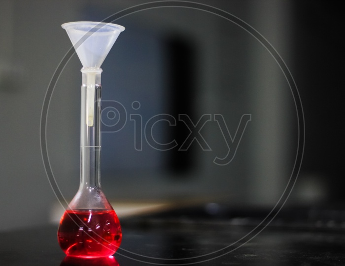 Red Liquid In A Round Bottomed Flask With Funnel On A Black Granite Table In Dark Background