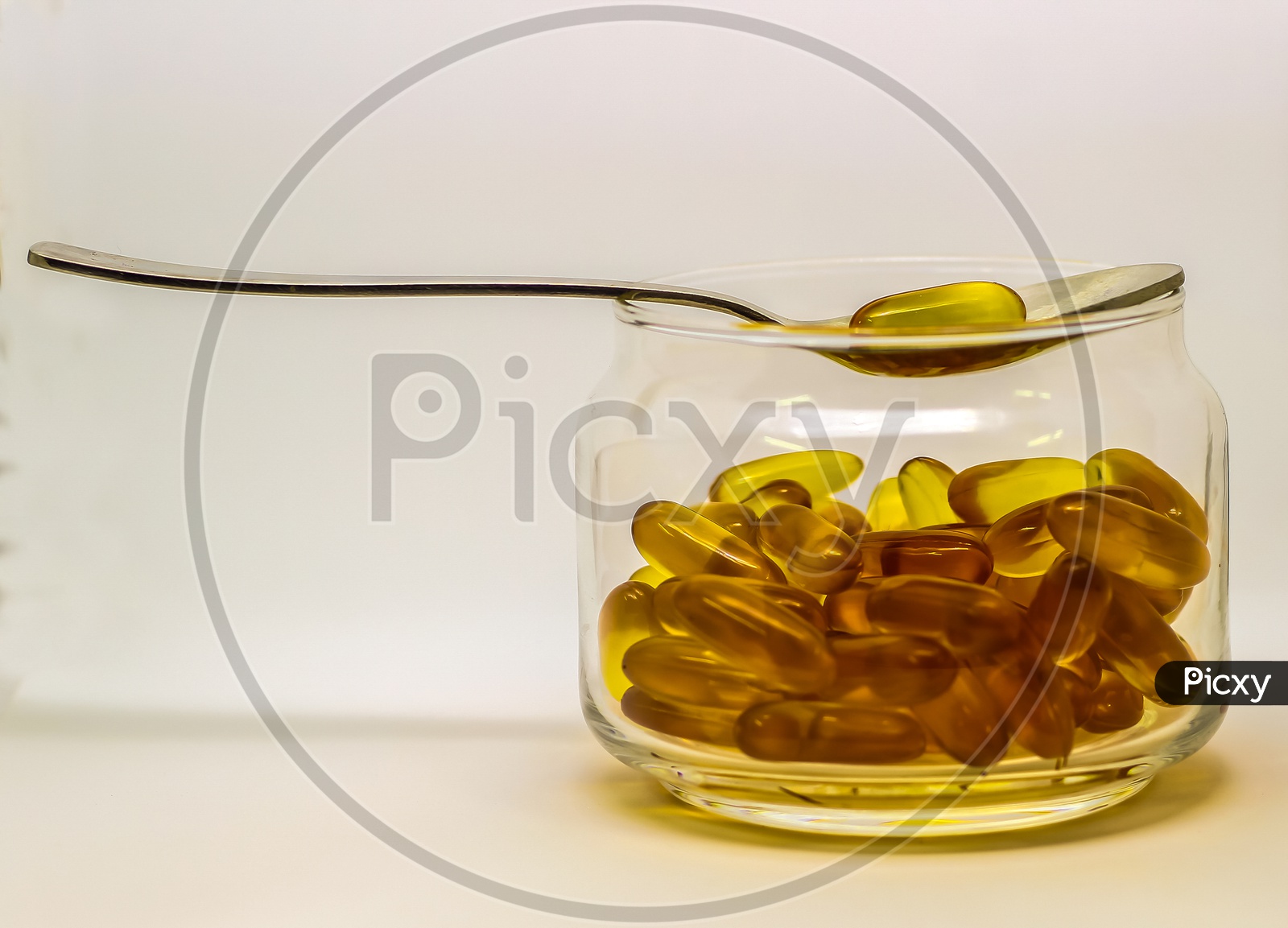 Cod Liver Oil Omega 3 Vitamin E Gel Capsules Isolated On White Background In A Transparent Glass Bottle With A Steel Spoon