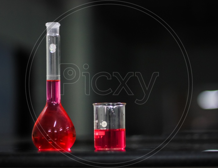 Red Liquid In A Round Bottomed Flask And Glass Beaker On A Black Granite Table In Dark Background