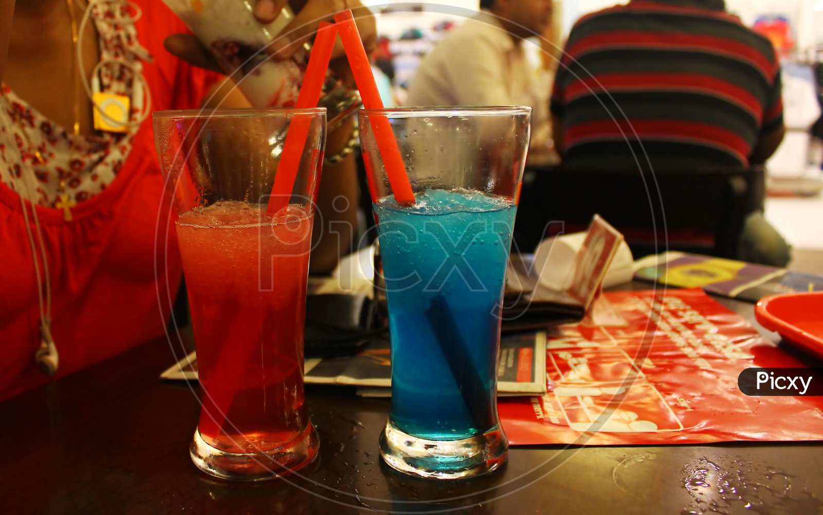 red and blue iced smoothie in long glasses with straws on table