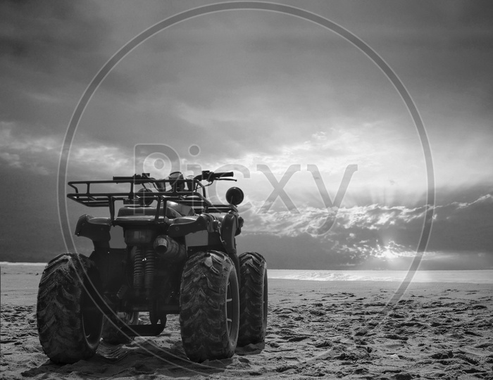 Four Wheeler Dirt Bike On Sand Of Sea Beach During Sunrise With Dramatic Colourful Sky, Black And White Photo