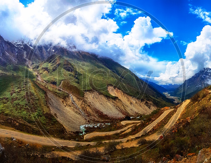 Panoramic View Of Hilly Road Among Mountains Landscape With White Clouds And Blue Sky