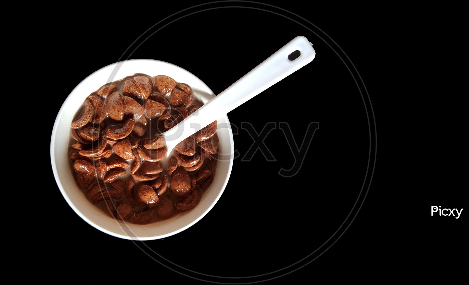 Chocolate Cornflakes Dipped In Chocolate Milk In A White Bowl With Spoon In Black Background