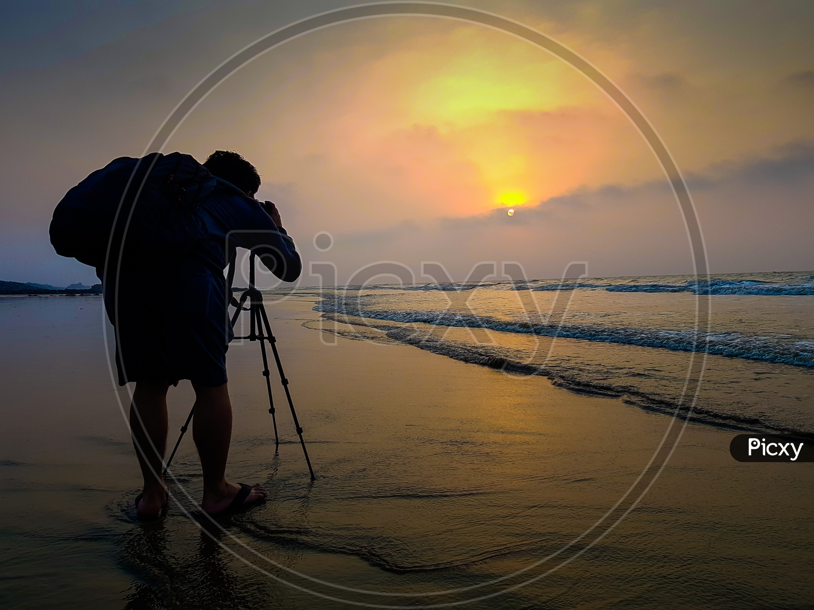 A Photographer With A Bagpack Taking Photo Of Sunrise At The Beach At Dawn
