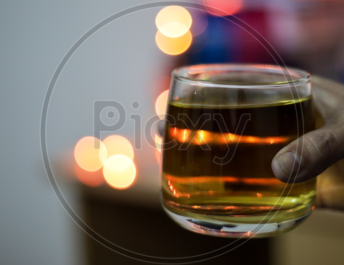 A Glass Of Alcohol Whisky Held In Hand With Background Blur Bokeh Lights