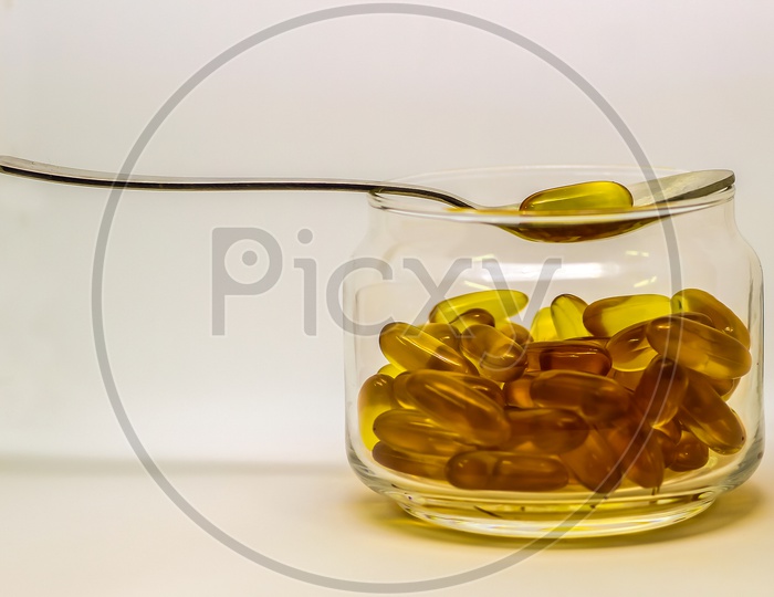 Cod Liver Oil Omega 3 Vitamin E Gel Capsules Isolated On White Background In A Transparent Glass Bottle With A Steel Spoon