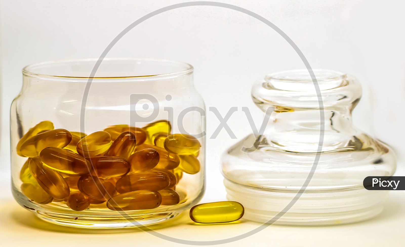 Cod Liver Oil Omega 3 Vitamin E Gel Capsules Isolated On White Background In A Transparent Glass Bottle With Glass Lid