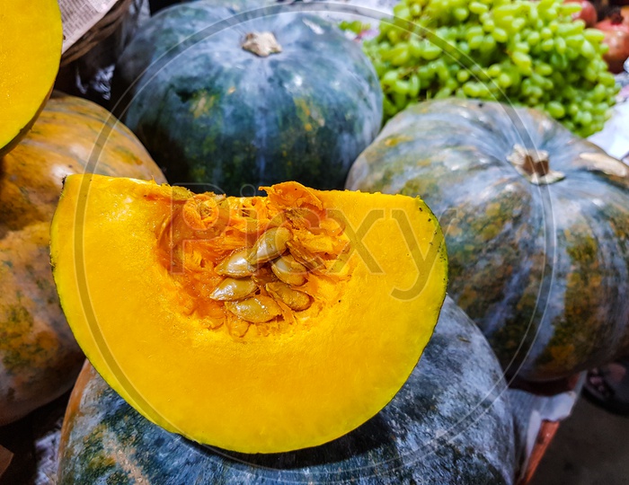 Fresh Pumpkin Cut Open To Show Yellow Interior In Background Of Heap Of Pumpkins In Vegetable Market For Sale