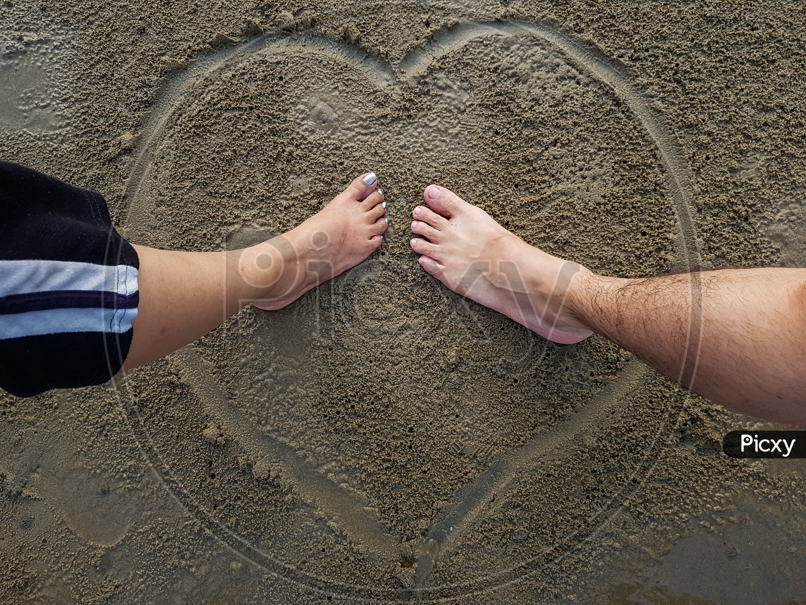 Romantic Couple Putting Feet Together On Heart Sign Background Drawn On Wet Beach Sand