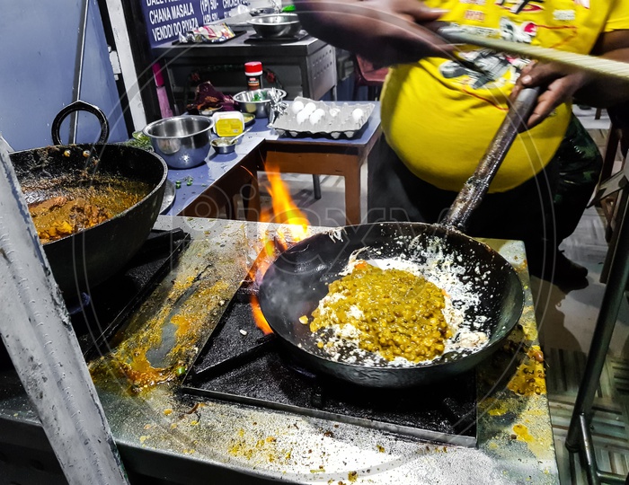 A Chef Cooking Tadka Fry In A Frying Pan At A Road Side Food Corner On A Stove Over Flames