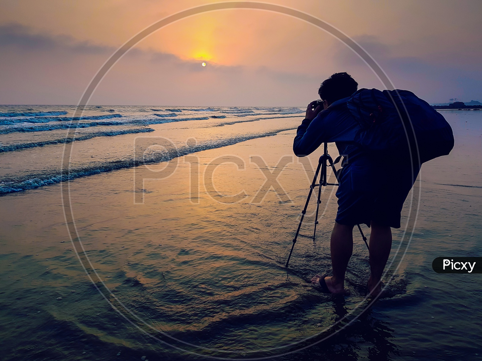 A Photographer With A Bagpack Taking Photo Of Sunrise At The Beach At Dawn