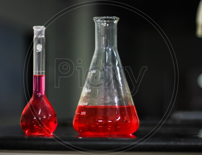 Red Liquid In A Conical Flask And Round Bottomed Flask On A Black Granite Table In Dark Background