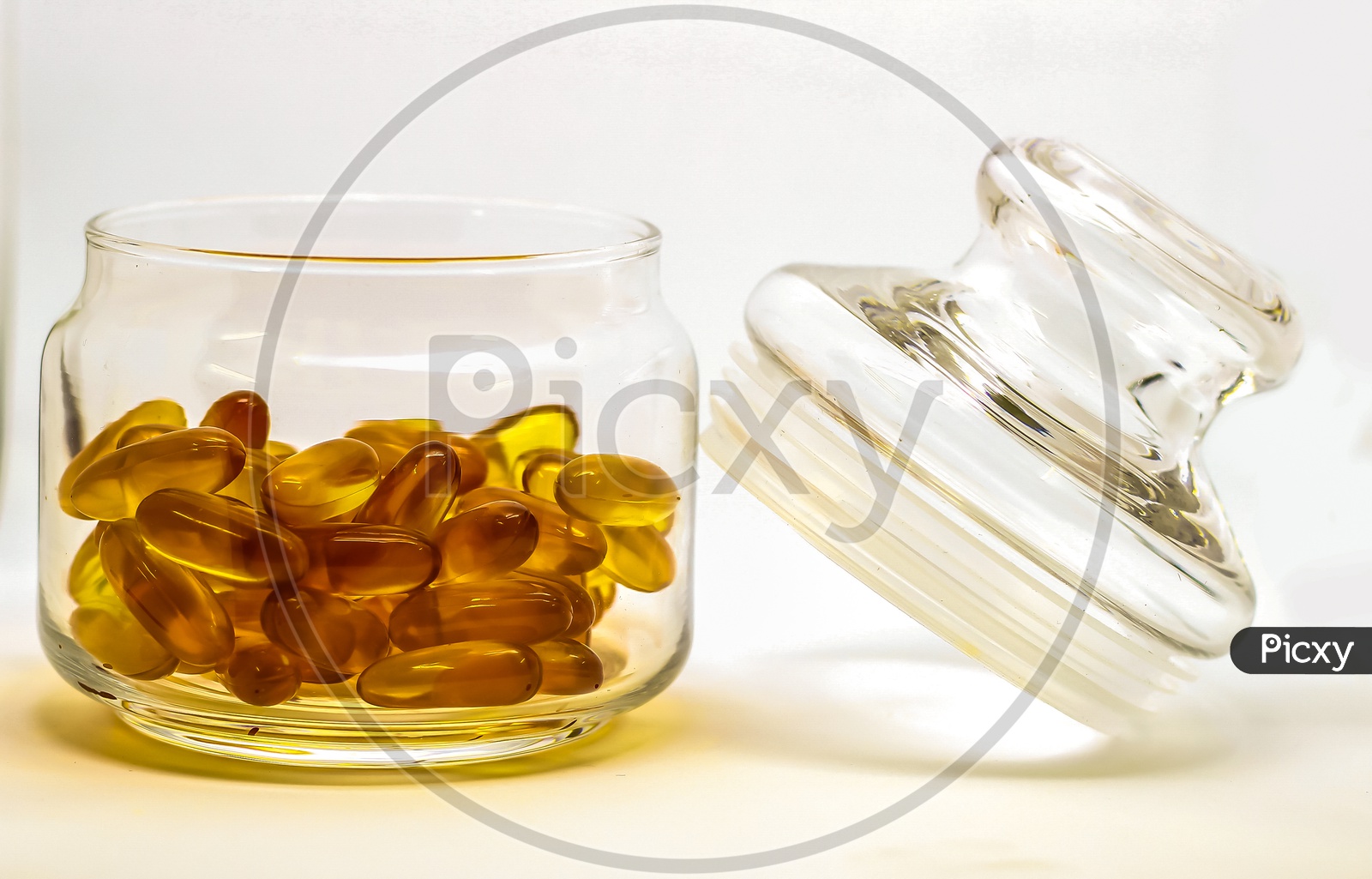 Cod Liver Oil Omega 3 Vitamin E Gel Capsules Isolated On White Background In A Transparent Glass Bottle With Glass Lid