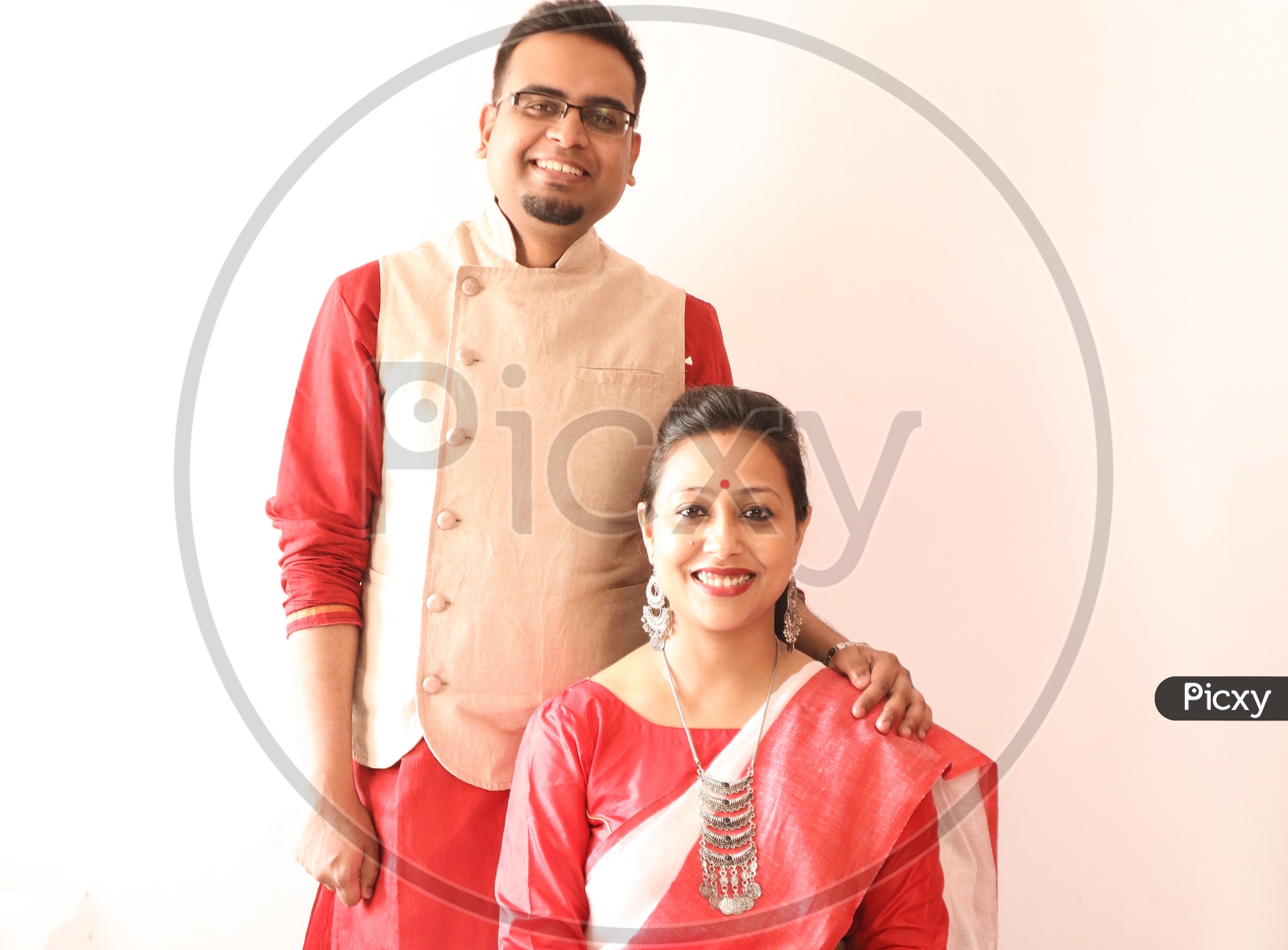 A Young Indian Bengali Assamese Married Couple Dressed In Red And White Ethnic Indian Dress And Smiling