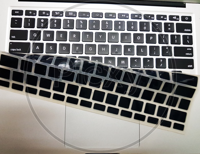 Silicon laptop keyboard cover raised with a hand to show underlying laptop isolated keys