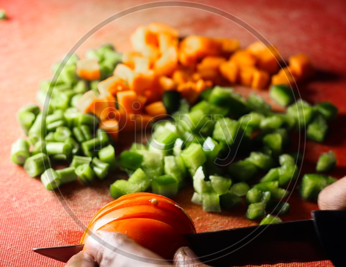 Capsicum Tomatoes And Carrot Cut Into Small Pieces,Finely Chopped Vegetables On A Chopping Board By Knife In Hand