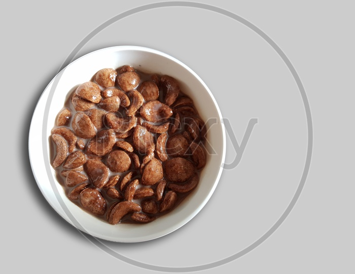 Chocolate Cornflakes Dipped In Chocolate Milk In A White Bowl In Light Background