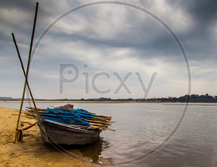 Landscape Of A Boar Tied At The Corner Of River Bed Sandy Beach And Cloudy Sky Day Time Scene.