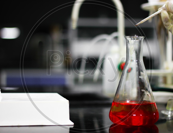 Pouring A Red Chemical On A Glass Conical Flask With A Dropper In A Chemistry Lab